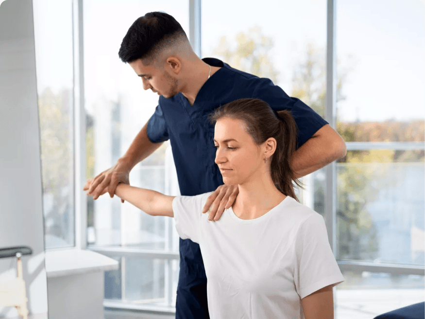 A therapist supporting a standing patient's arm through a shoulder range-of-motion exercise