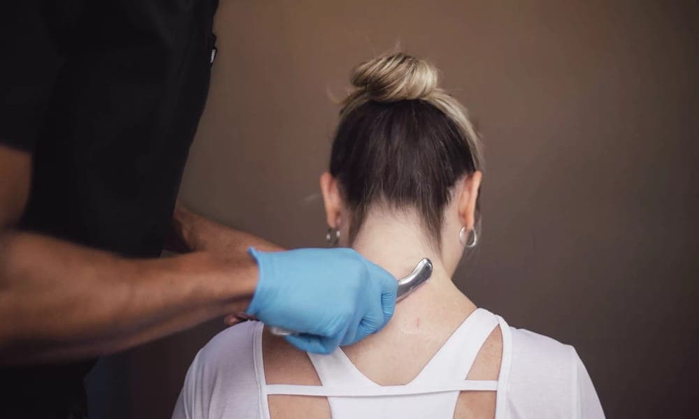 A gloved clinician drawing a Graston instrument along the back of a patient's neck