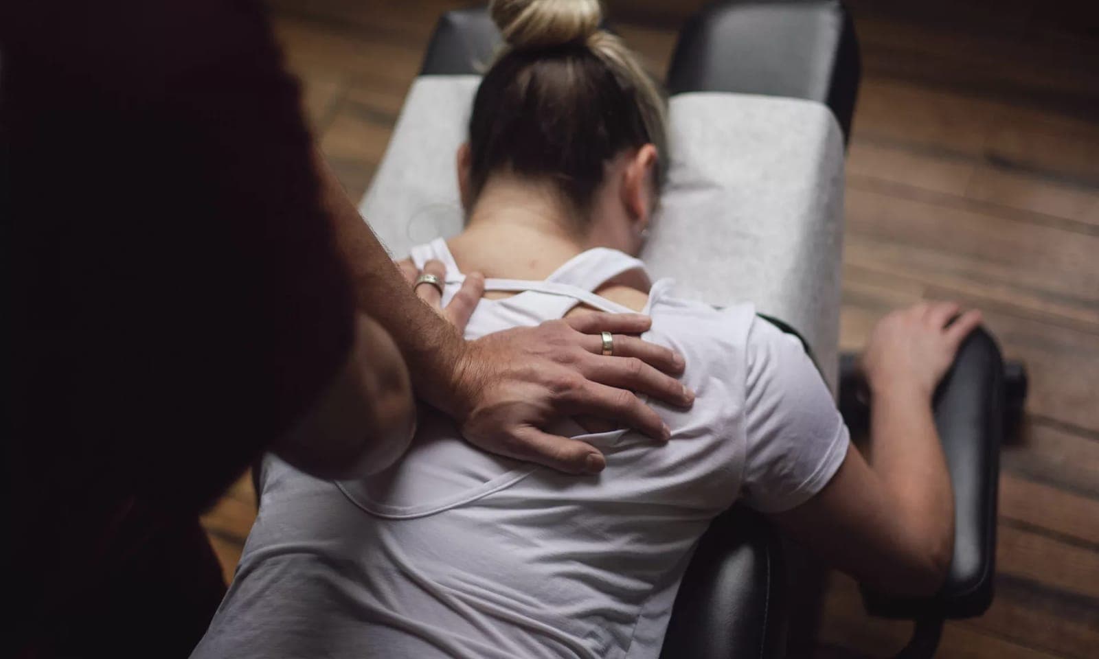 A chiropractor pressing one hand between the shoulder blades of a patient lying face down on a treatment table