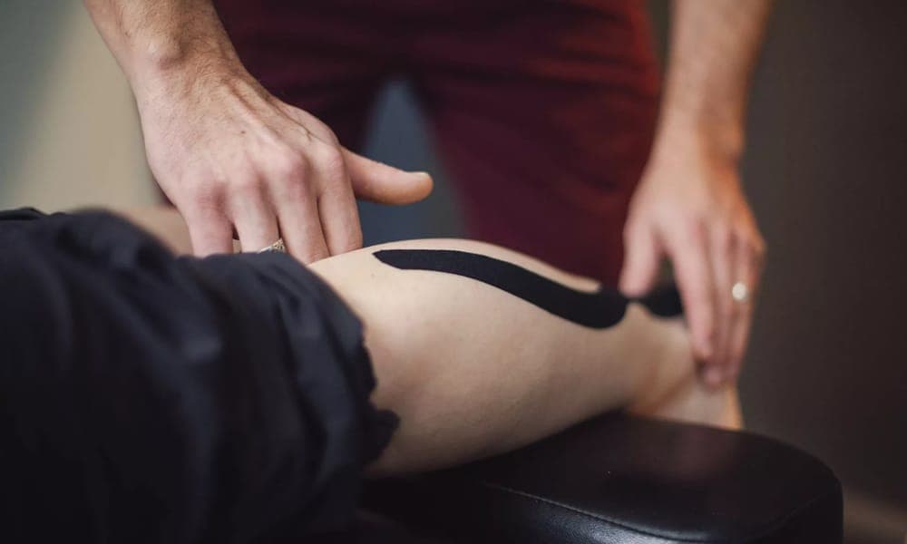A clinician smoothing a strip of kinesiology tape along a patient's thigh