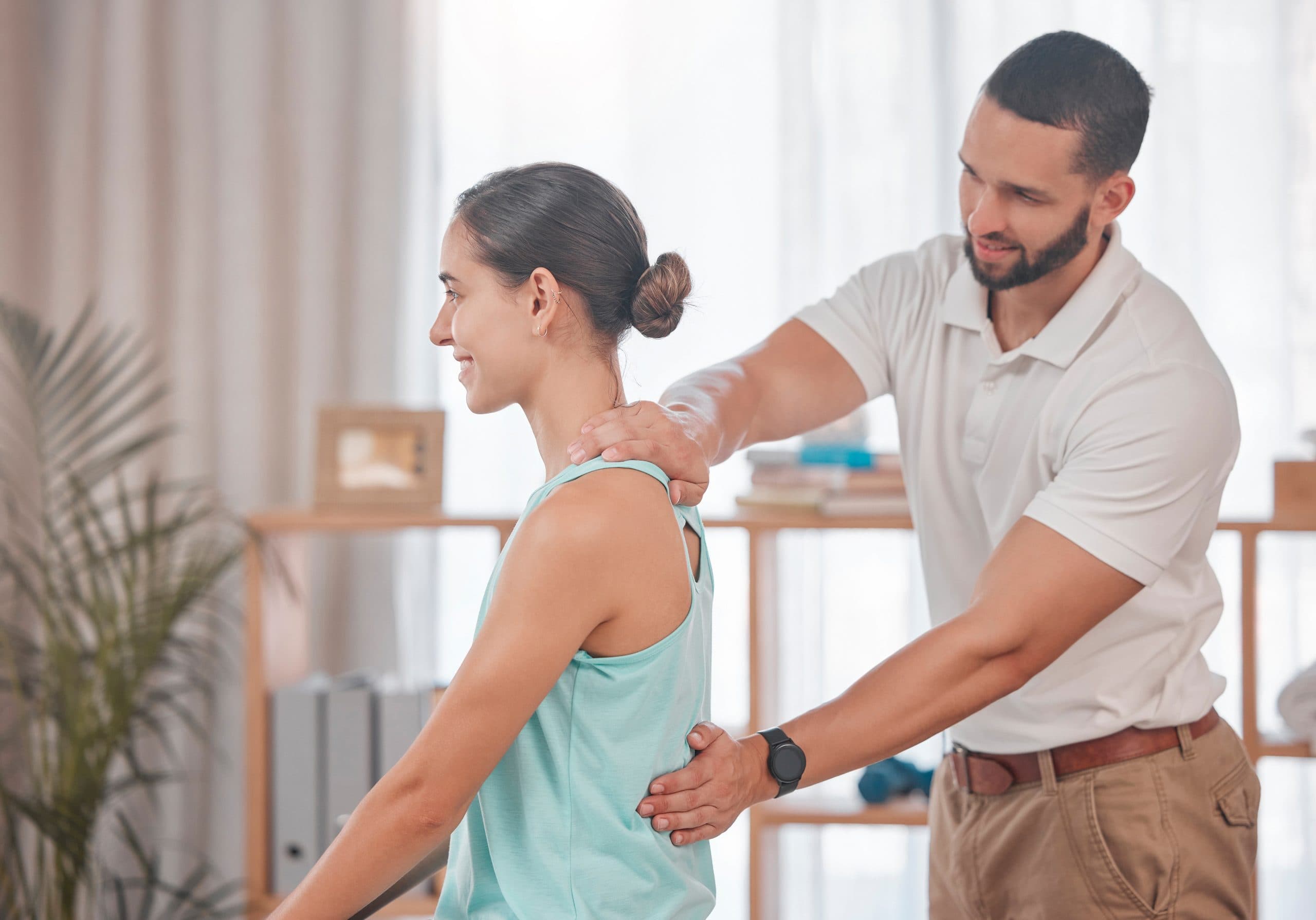 A clinician applying pressure along a patient's shoulder and mid-back while she extends both arms behind her