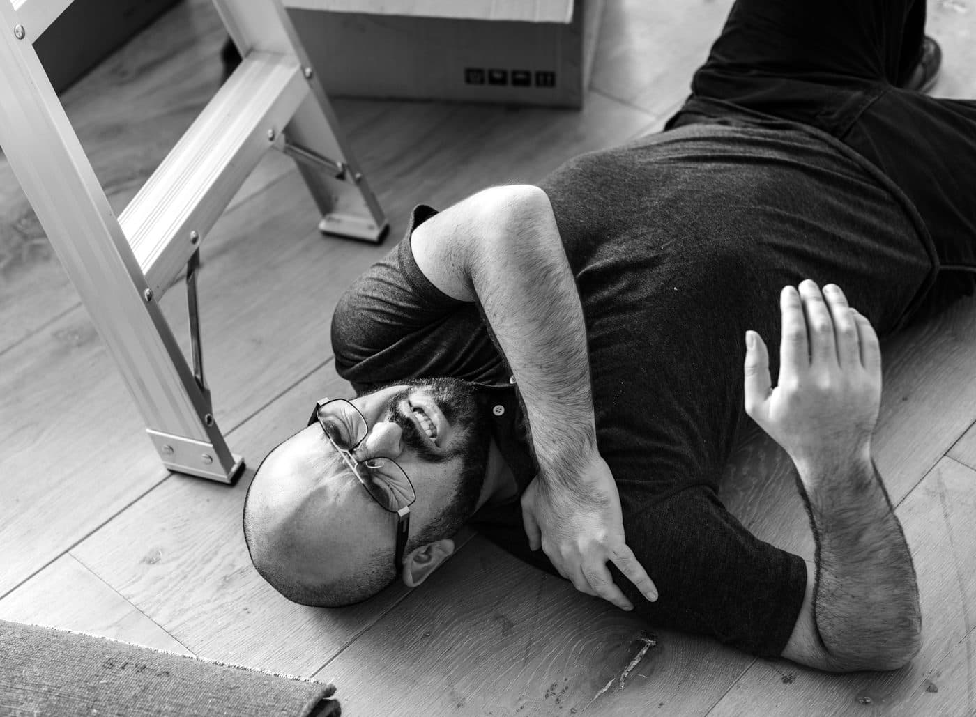 A man on the floor beside a step ladder holding his shoulder in pain after a fall