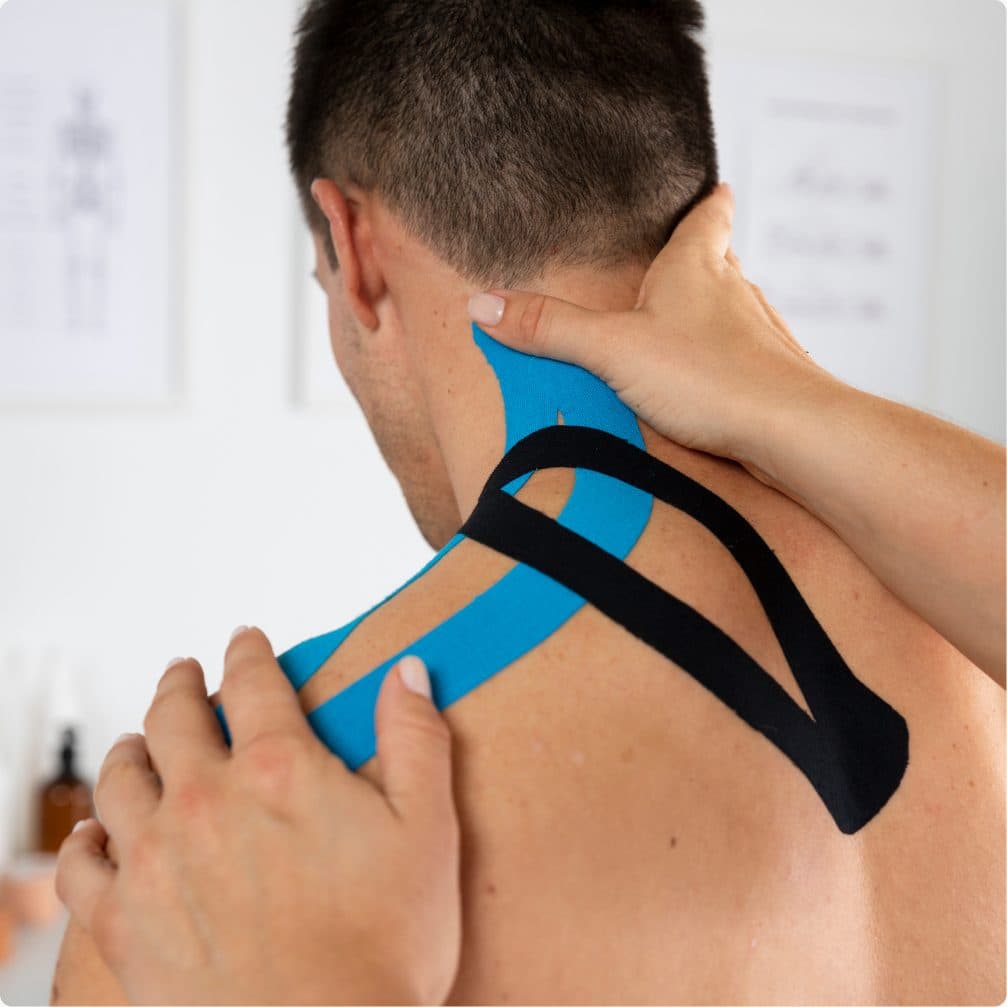 Blue and black kinesiology tape applied across a man's neck and shoulder while a practitioner presses it into place