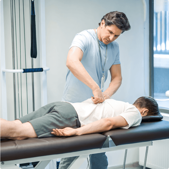 A clinician applying manual pressure along the lower spine of a patient lying face down on a treatment table