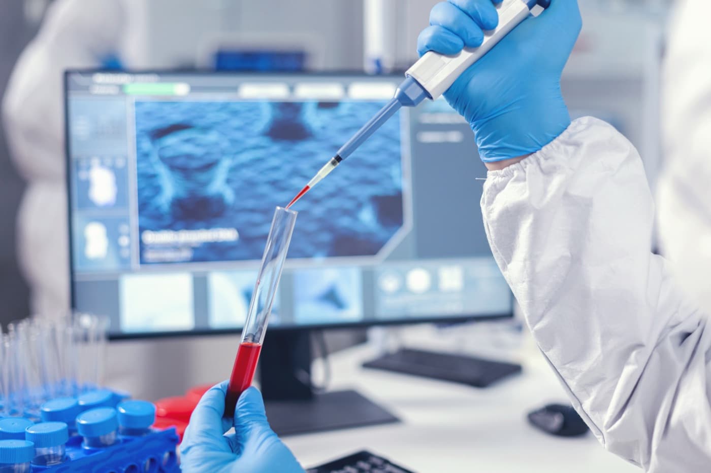 A gloved lab technician pipetting a sample in front of a genetic analysis screen