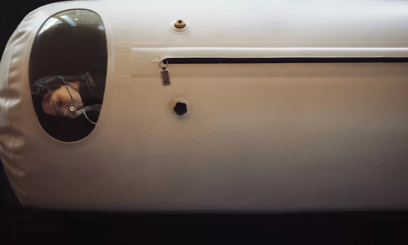 A patient lying inside a hyperbaric oxygen chamber, seen through the porthole window