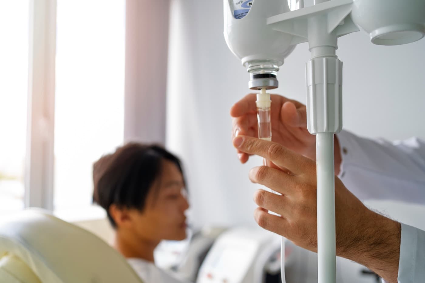 A clinician adjusting the flow regulator on an IV line above a seated patient
