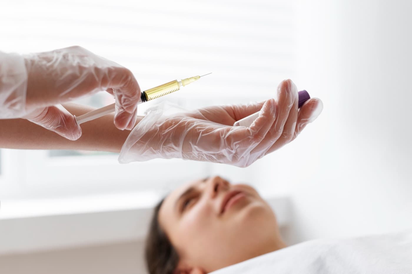 A gloved clinician drawing up a syringe above a patient lying on a treatment table