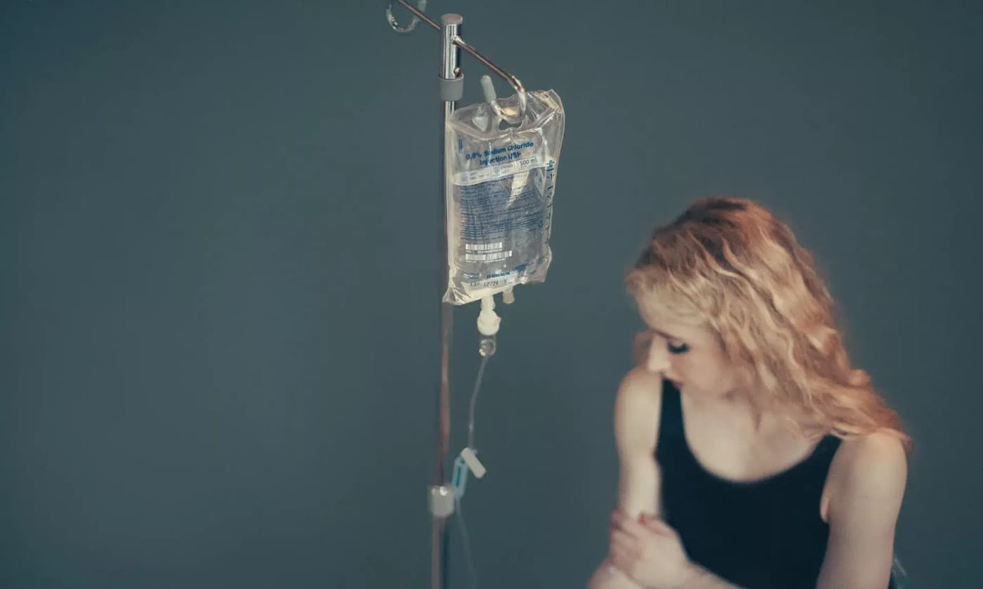 A patient seated beside an IV drip stand during a vitamin infusion