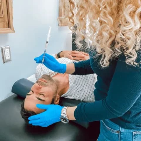 A clinician in blue gloves steadying a patient's head while administering treatment on a treatment table