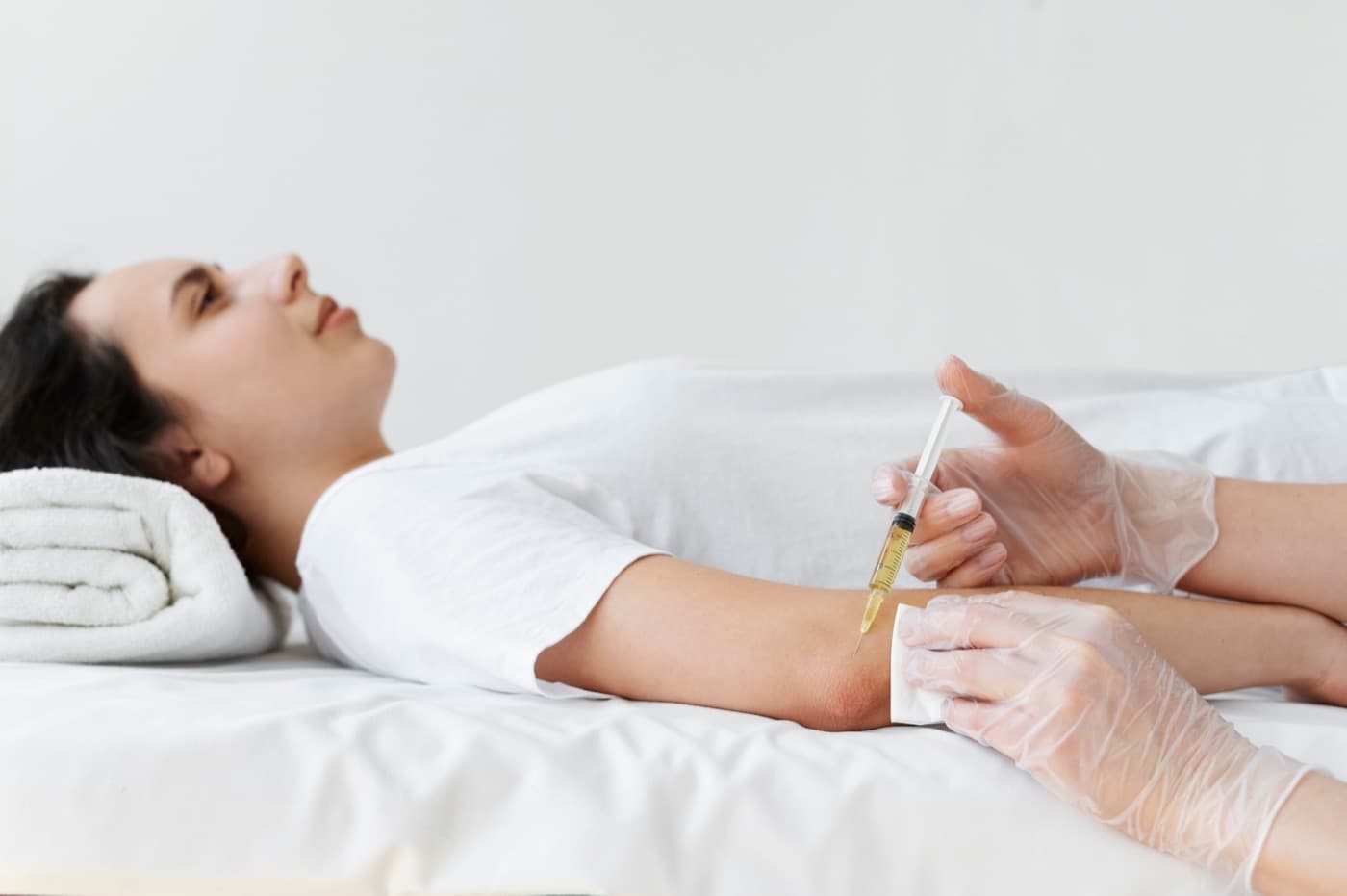 A woman lying on a treatment table while a gloved clinician gives an injection into her forearm