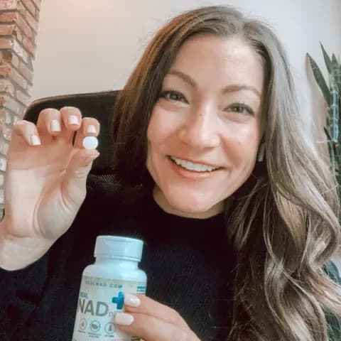 A smiling woman holding a white dissolvable tablet beside a bottle labelled NAD+