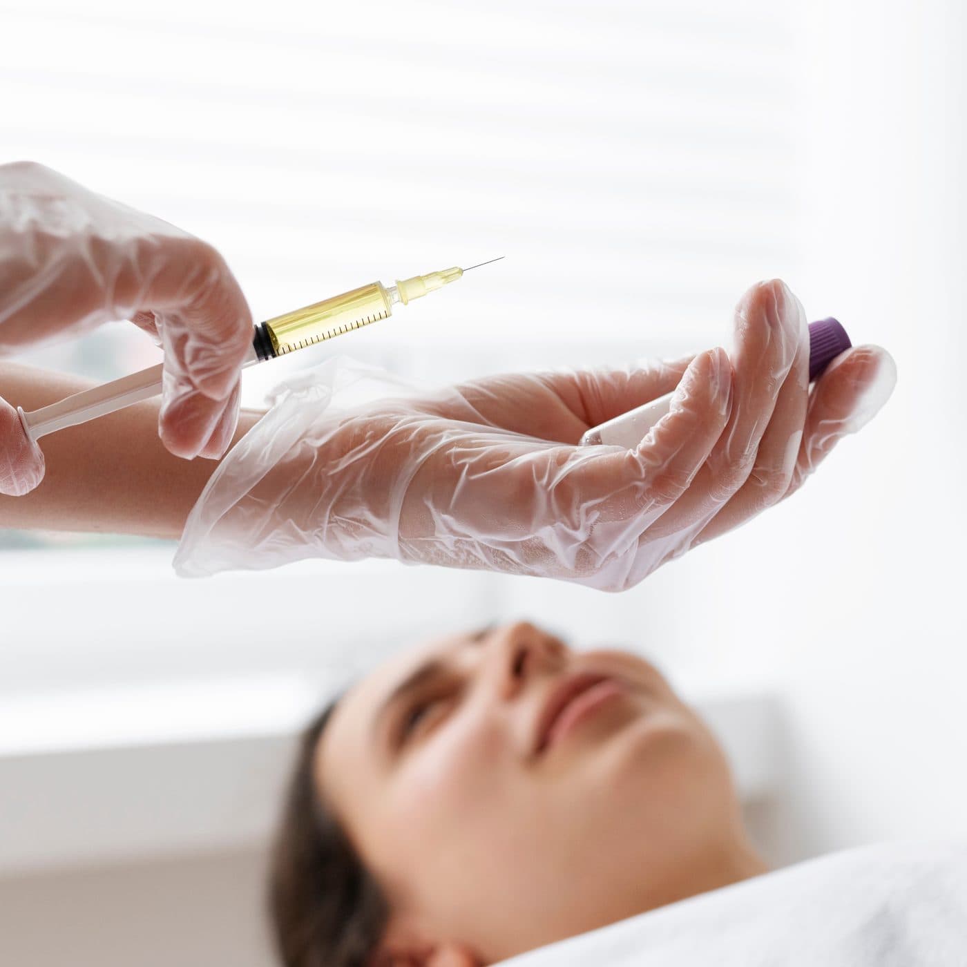 A clinician in clear gloves preparing a fine syringe above a patient resting on a treatment table