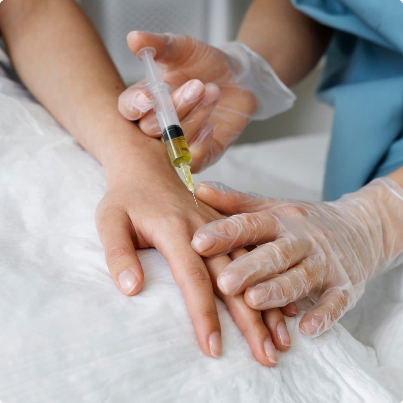 Gloved clinical hands steadying a patient's hand while placing a needle in the back of it