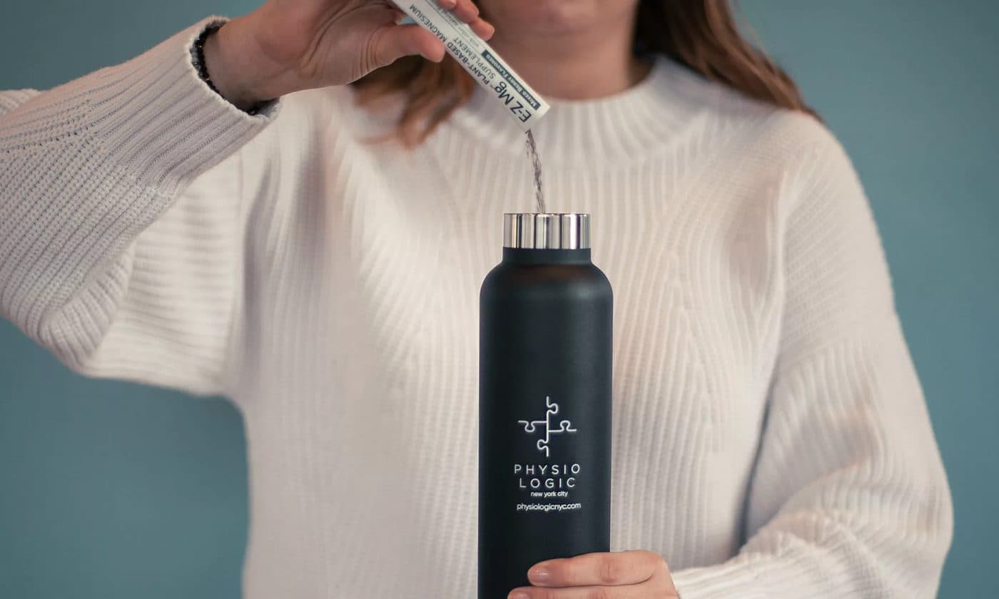 A person in a knit sweater holding a black Physio Logic water bottle