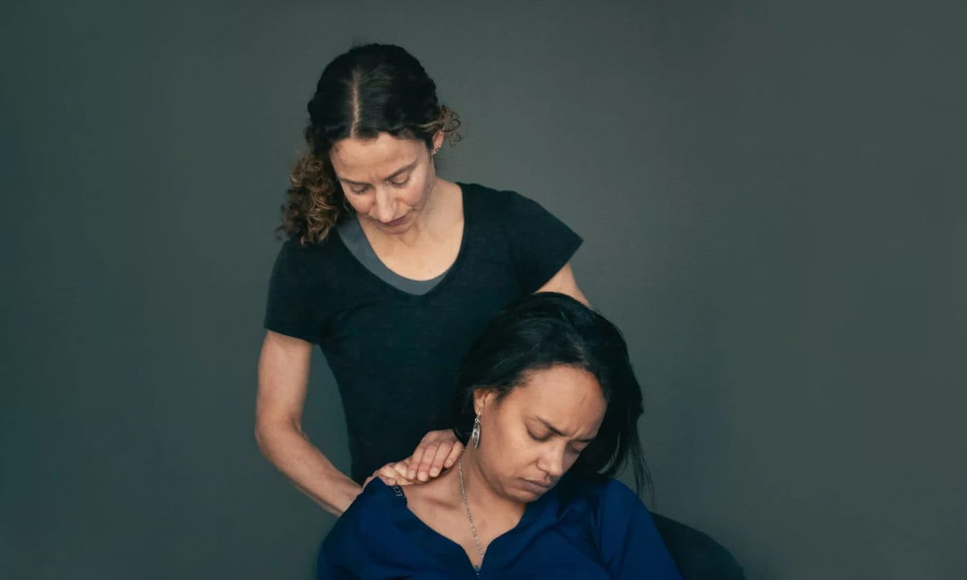 A therapist applying pressure to a seated patient's shoulder while the patient turns their head away
