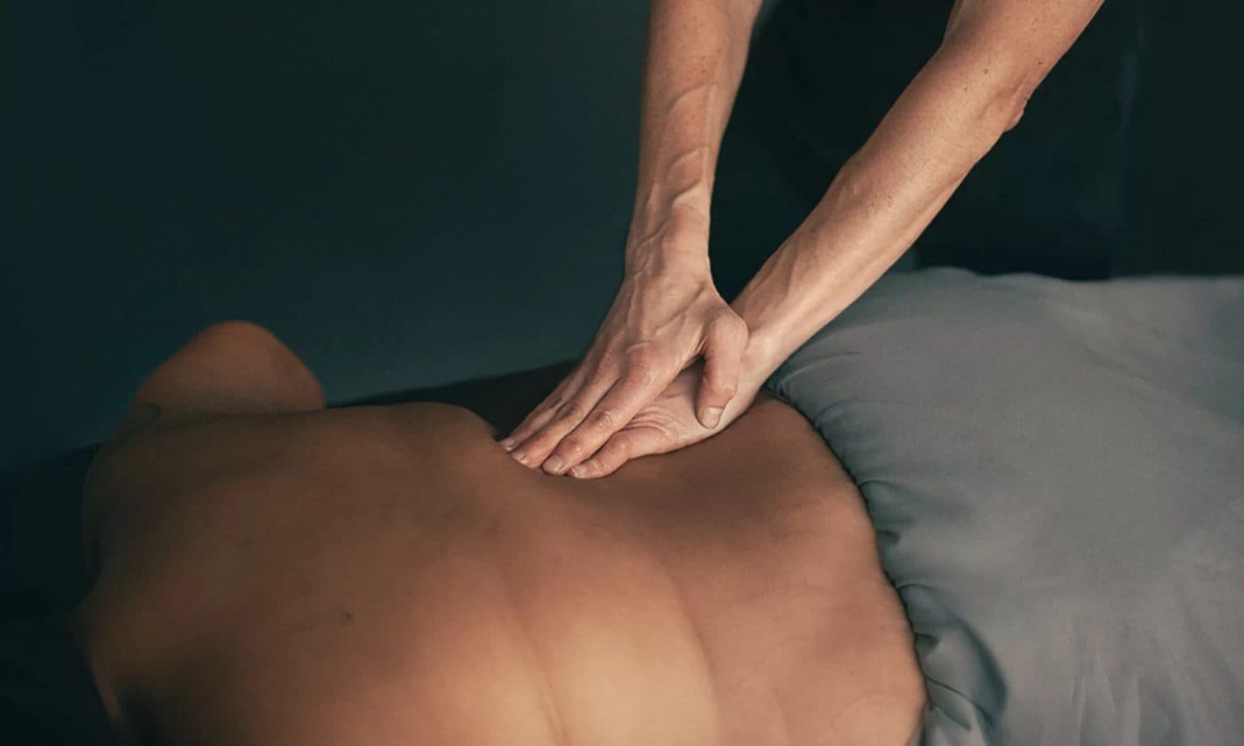 Close-up of a therapist's hands pressing along the muscles beside a patient's spine