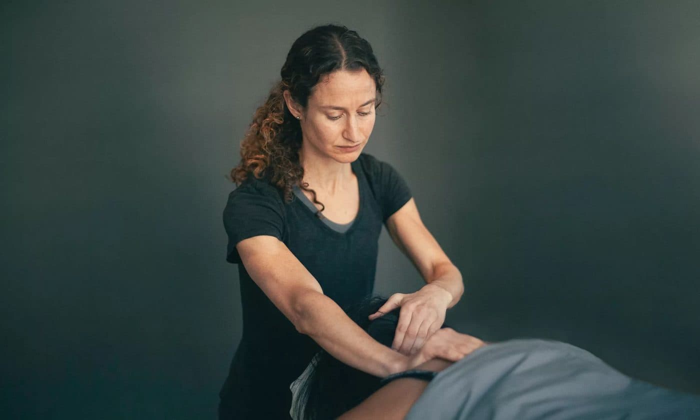 A massage therapist leaning into a patient's upper back with both hands on a treatment table