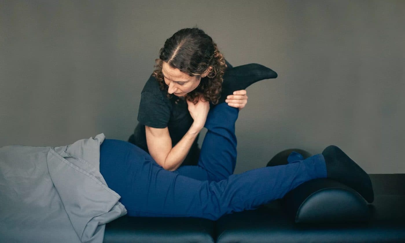 A therapist holding a side-lying patient's bent knee and hip through a stretch on a treatment table