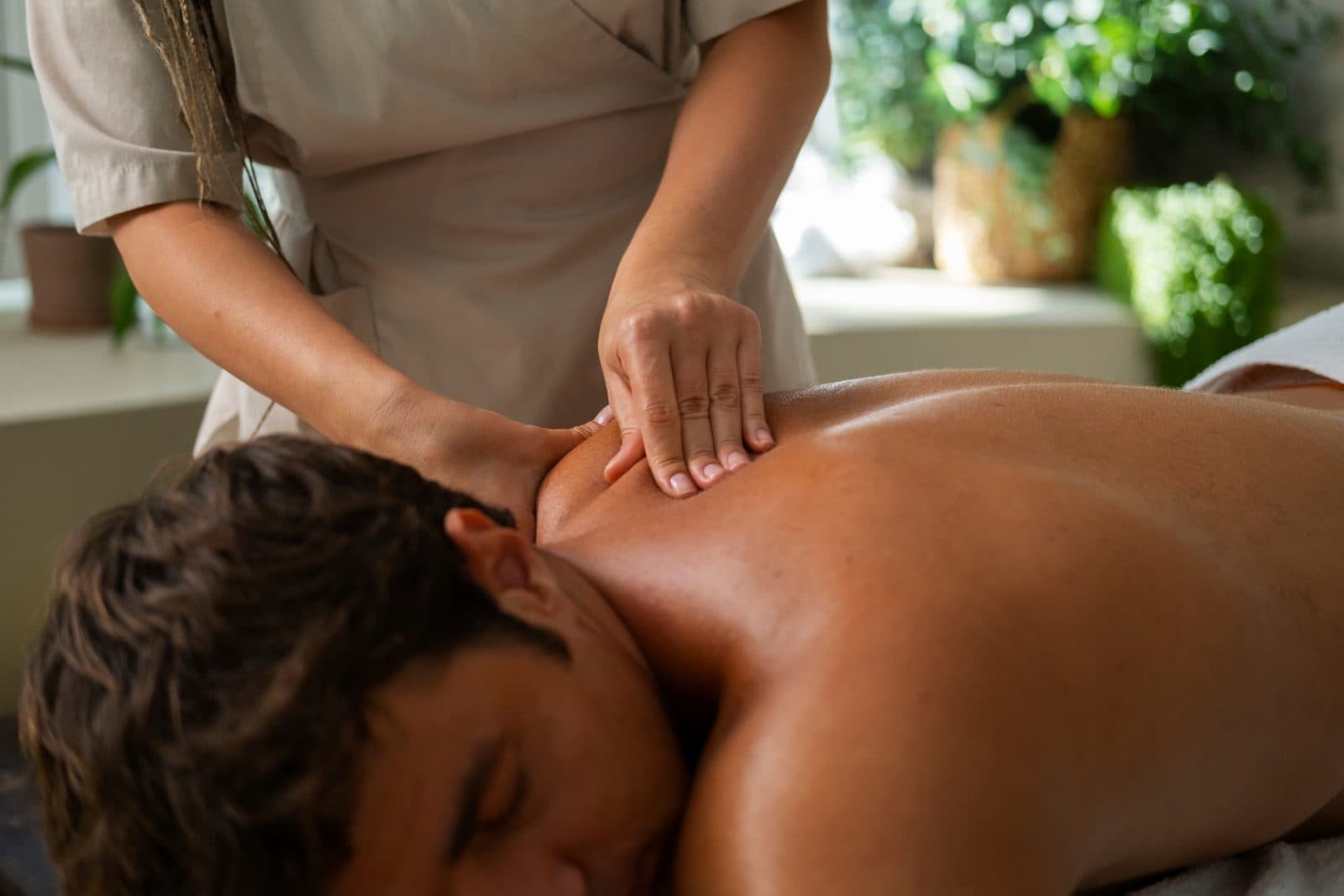 A massage therapist gripping the shoulder and upper trapezius of a patient lying face down on a treatment table