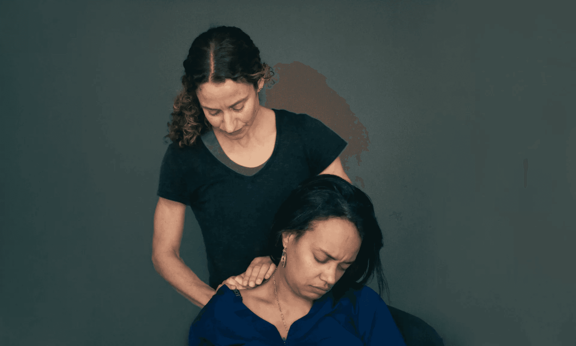 A therapist standing behind a seated patient, applying pressure to the side of the patient's neck