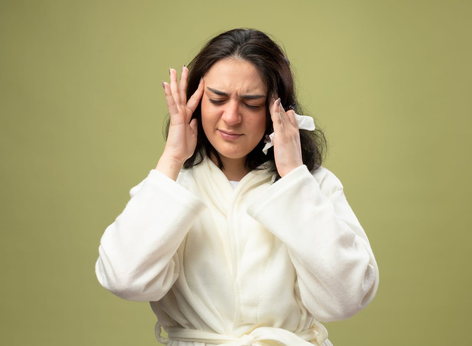 A woman in a white robe pressing her fingertips to her temples with her eyes closed during a migraine
