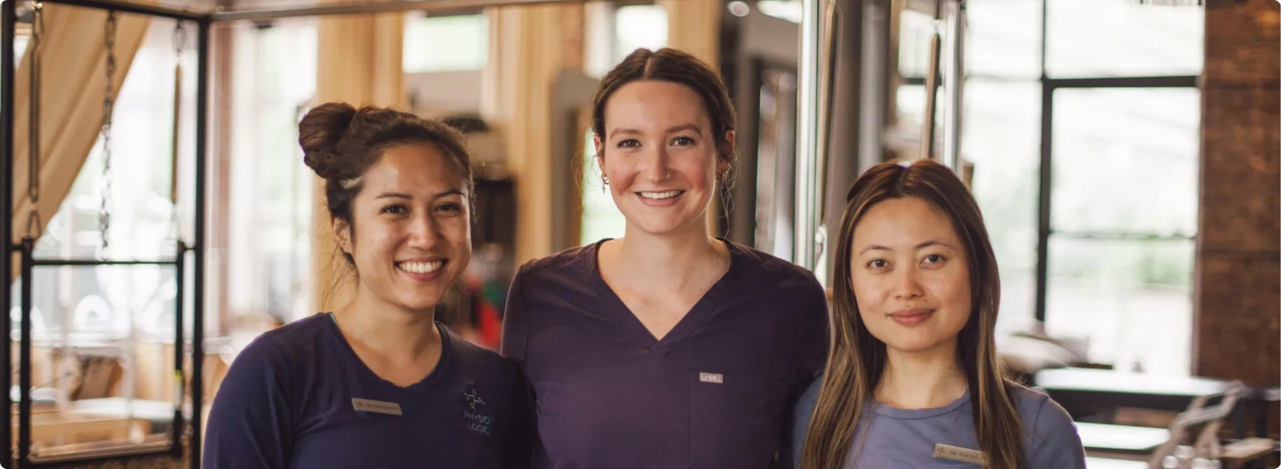 Three Physio Logic clinicians in purple scrubs smiling together in the Brooklyn studio