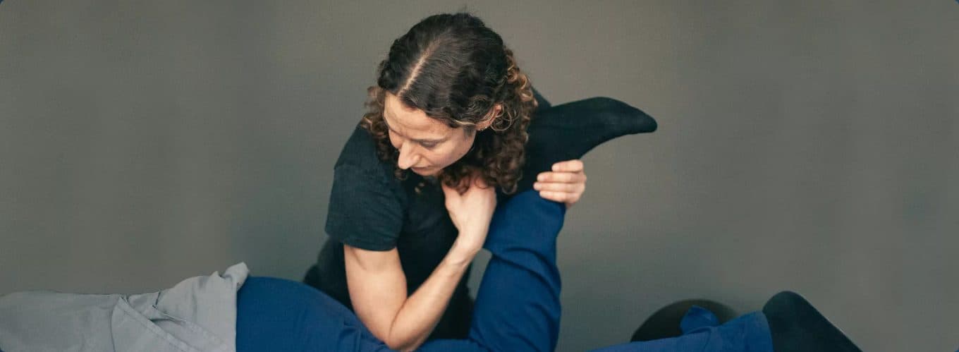 A physical therapist mobilizing a patient's hip and knee during a hands-on treatment session