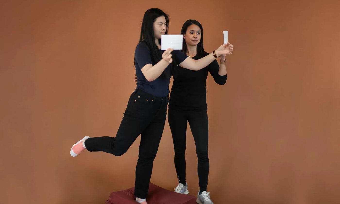 A therapist holding a gaze-stabilization card while a patient balances on one leg