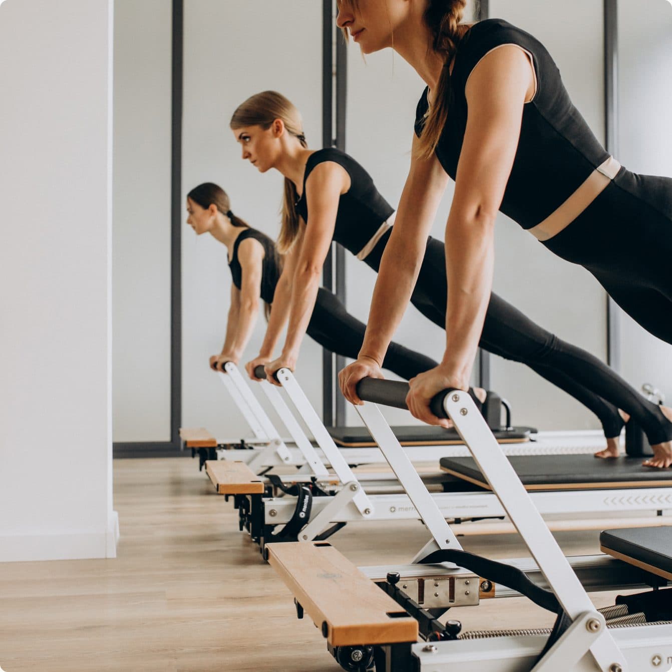 Three people holding a plank position on Pilates reformers in a bright studio
