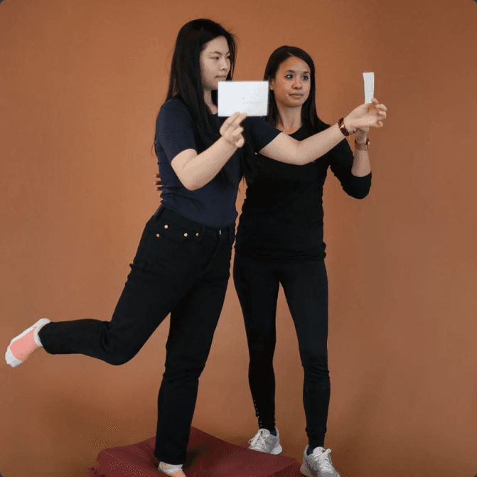 A patient balancing on one leg on a soft pad while a therapist holds a visual target at eye level