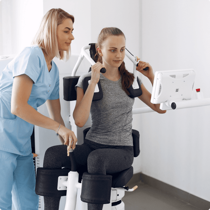 A clinician in blue scrubs guiding a seated patient through a supported balance-retraining machine