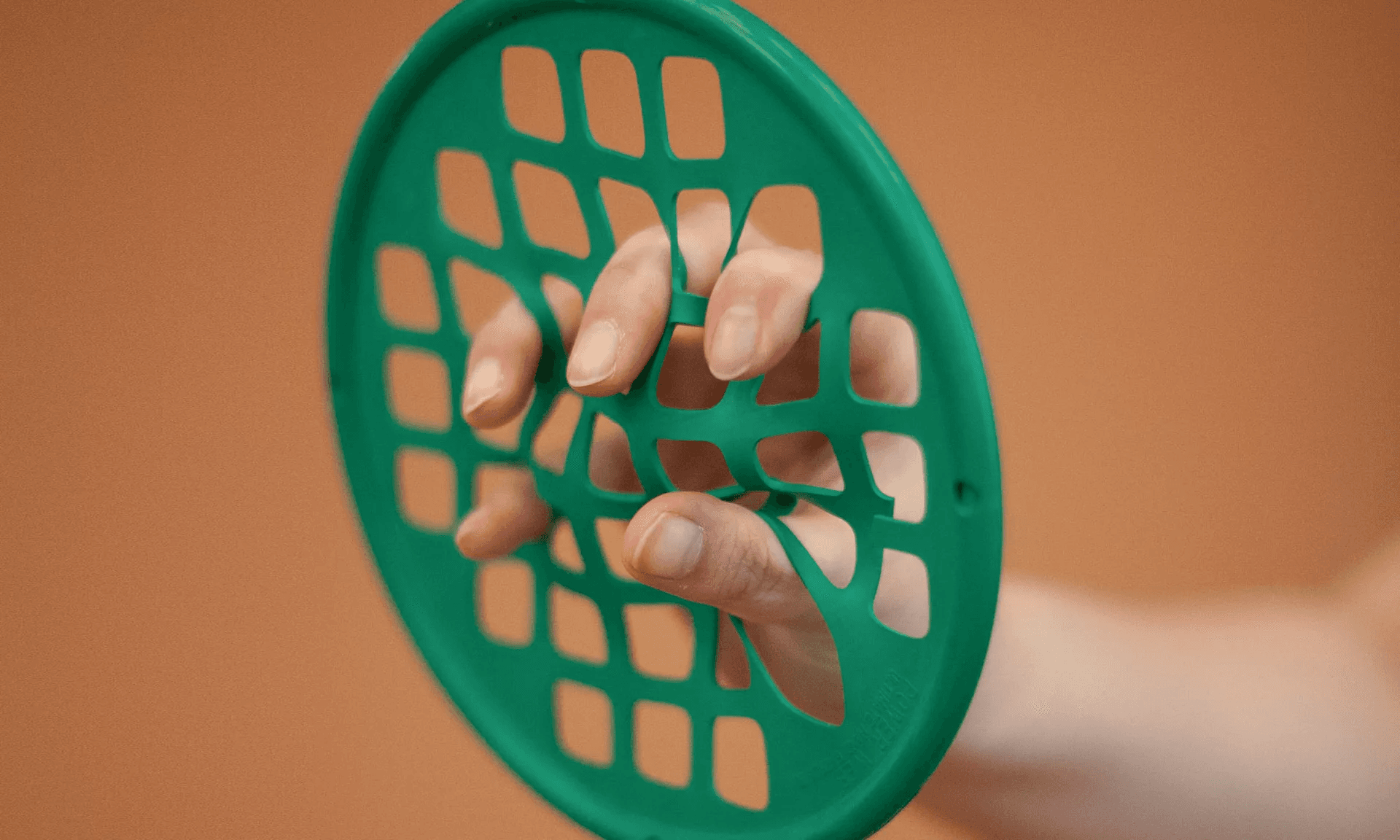 A patient's fingers stretching against a green hand-exerciser web