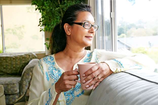 A woman in her fifties sitting by a window holding a mug