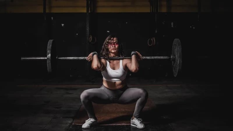 A woman performing a barbell back squat in a dimly lit gym