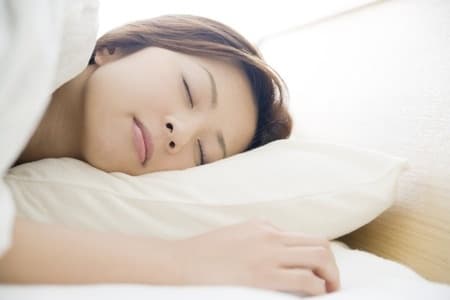 A person asleep on their side with their head resting on a white pillow