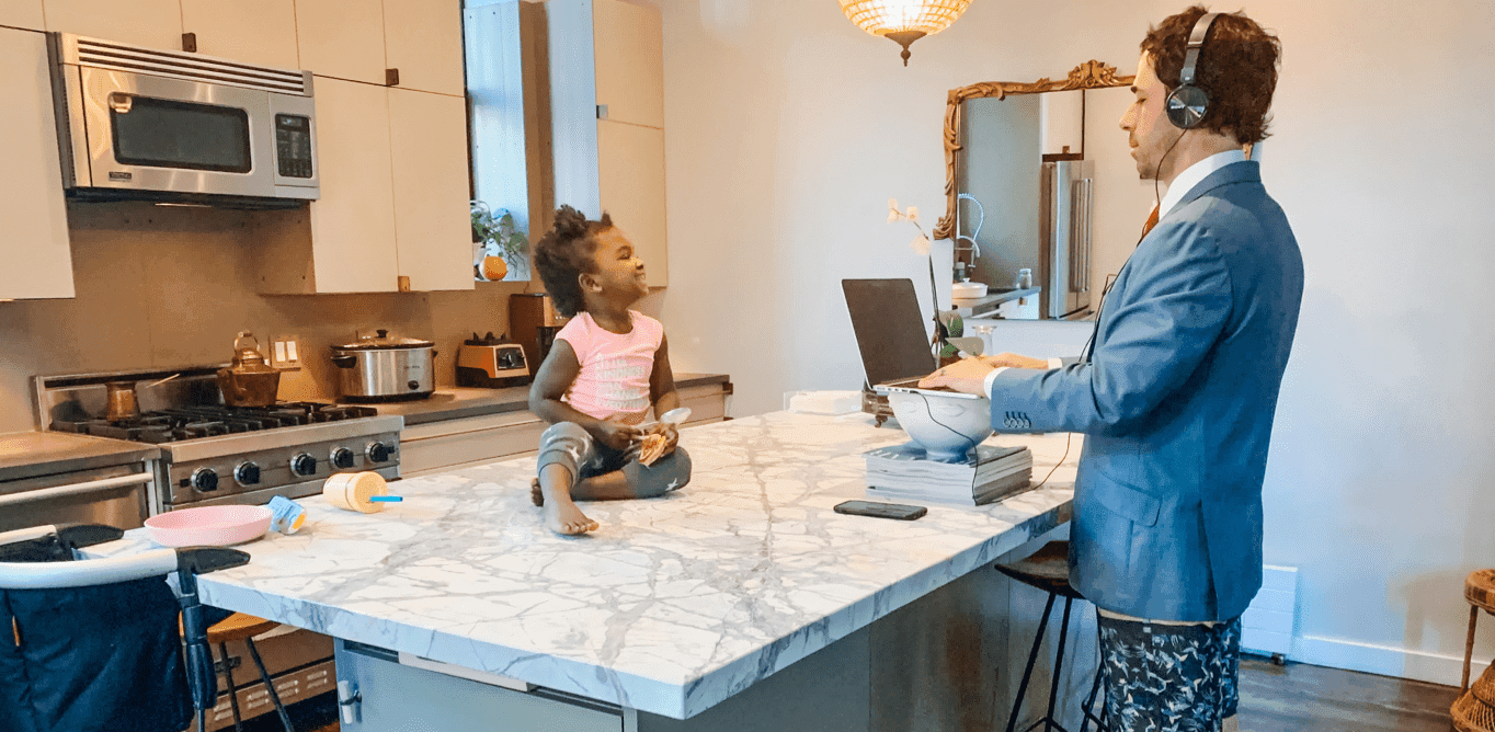 A parent working on a laptop at a kitchen island while a toddler plays on the counter