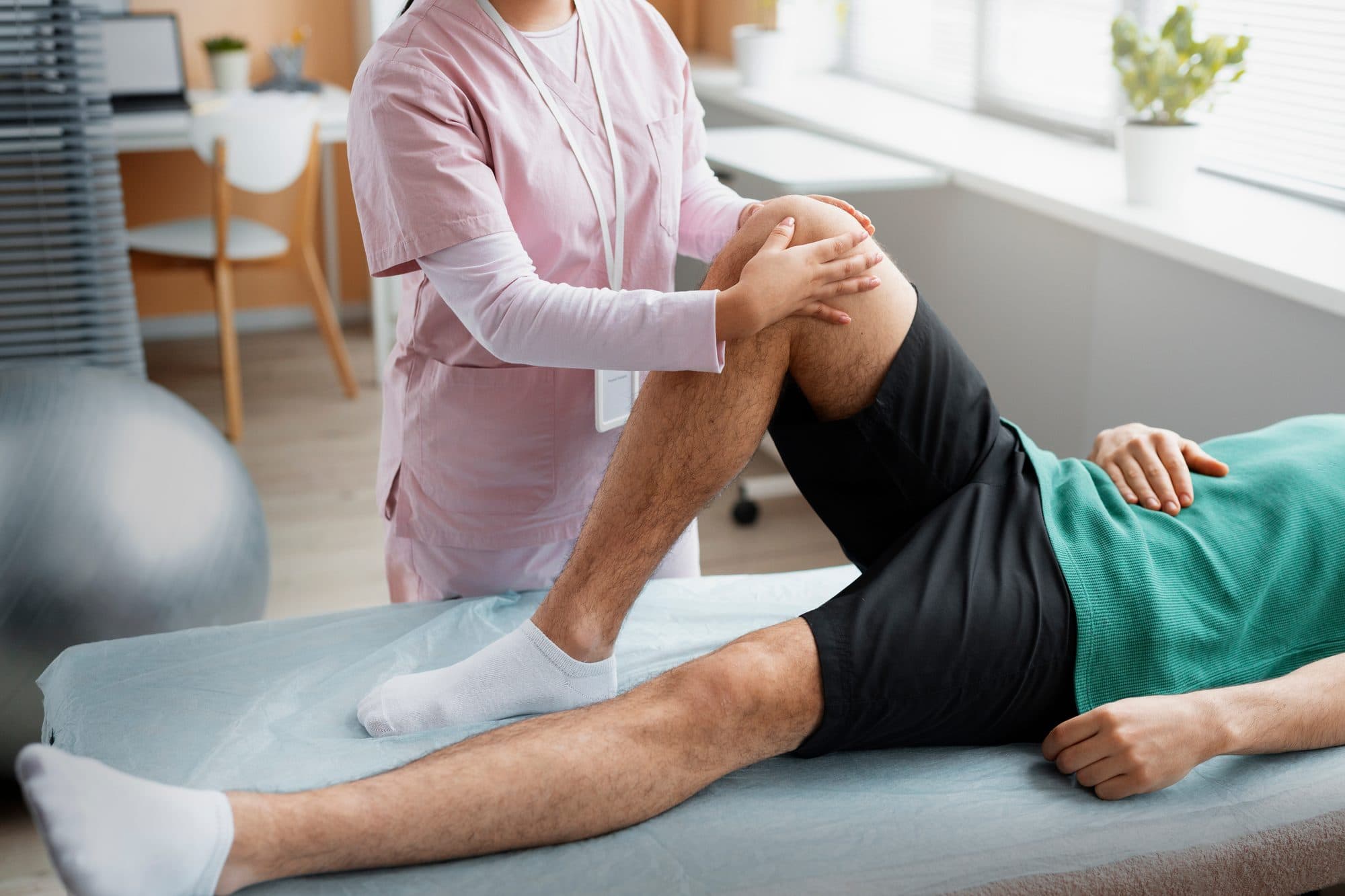 A Physio Logic therapist supporting a patient's knee through a guided range-of-motion exercise on a treatment table
