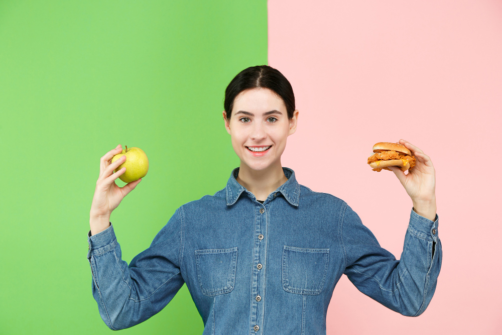 Woman holding an apple in one hand and a burger in the other, symbolizing food choices.